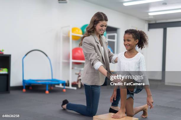 therapist doing stretching exercise with young african american girl - bare feet kneeling girl stock pictures, royalty-free photos & images