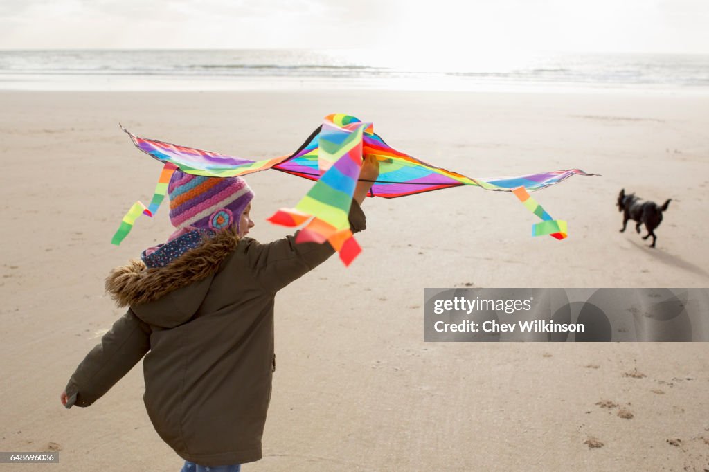 Young Girl holding a kite running on a beach with a dog