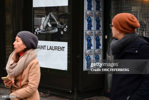 People pass an advertisement for the French luxury fashion brand Yves Saint Laurent on March 6, 2017 on the Champs Elysees in Paris. A new publicity...