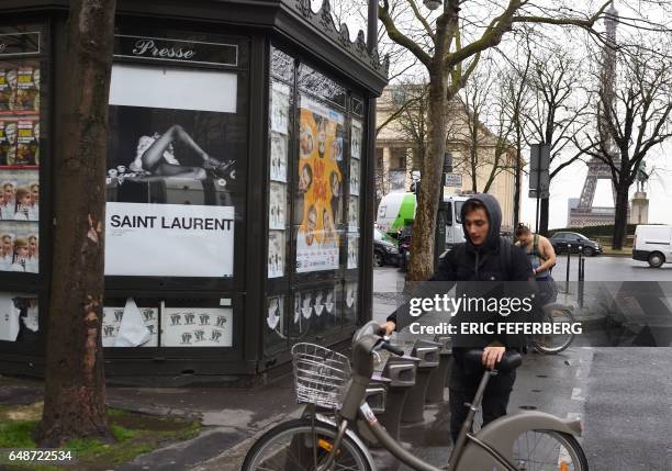 People parks bicycles next to an advertisement for the French luxury fashion brand Yves Saint Laurent on March 6, 2017 in Paris. A new publicity...