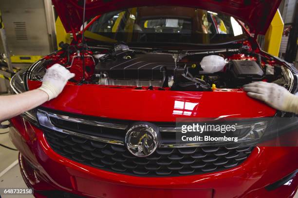Workers fit the front grill and badge panel to a red Vauxhall Astra vehicle on the production line at the Opel automobile plant in Gliwice, Poland,...