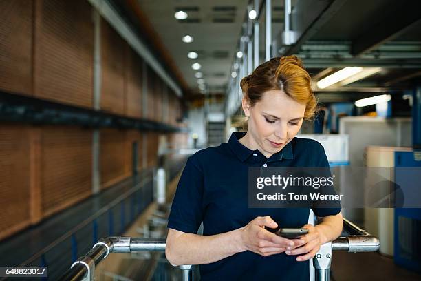 female worker in a factory checking smart phone - blue polo shirt photos et images de collection