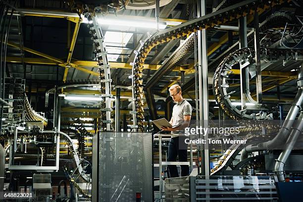 engineer with laptop in a factory between machines - industria foto e immagini stock