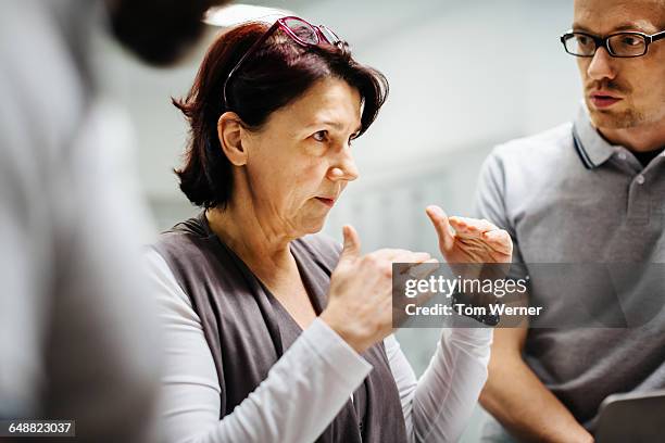 mature businesswoman briefing staff - leanincollection stock pictures, royalty-free photos & images