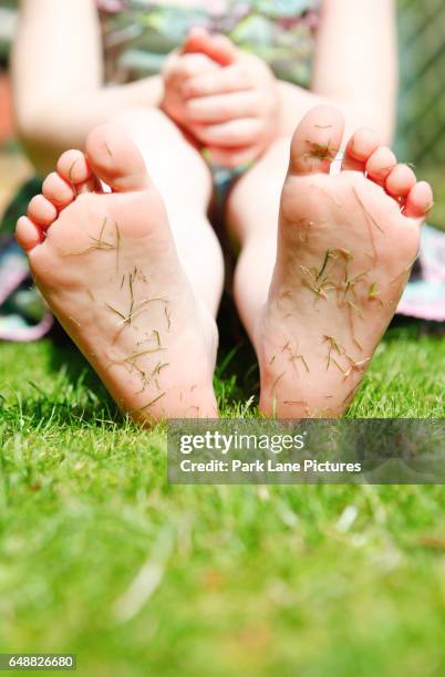 four year old girl in a garden with grass cuttings on the soles of her feet. - ent stockfoto's en -beelden