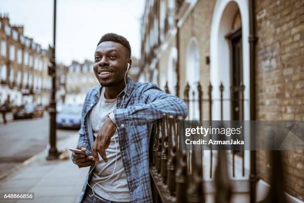 londen-stijl - young man listening to music on smart phone outdoors stockfoto's en -beelden