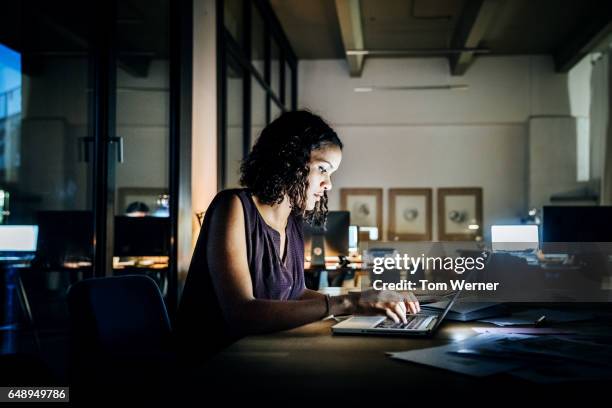 casual young businesswoman working late on a laptop - working overtime stock pictures, royalty-free photos & images