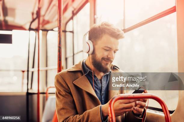 charming man listening to music with headphones on a public bus - man riding bus stock pictures, royalty-free photos & images