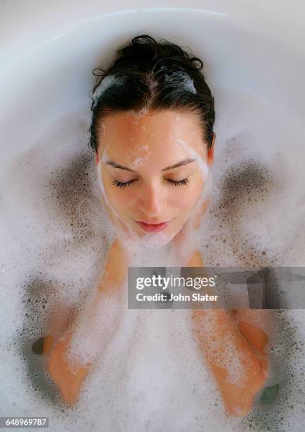 young woman washing her face in bath with bubbles - woman bath tub wet hair stock pictures, royalty-free photos & images