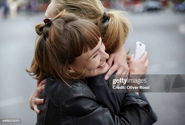 two female friends with cell phone hugging - omhelzen stockfoto's en -beelden