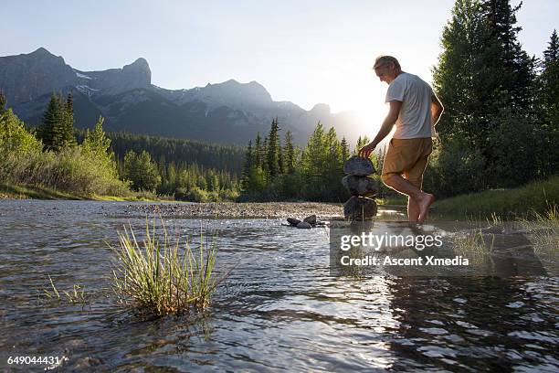 man puts final touches on zen rock stack, mtns - balanced rock stock-fotos und bilder