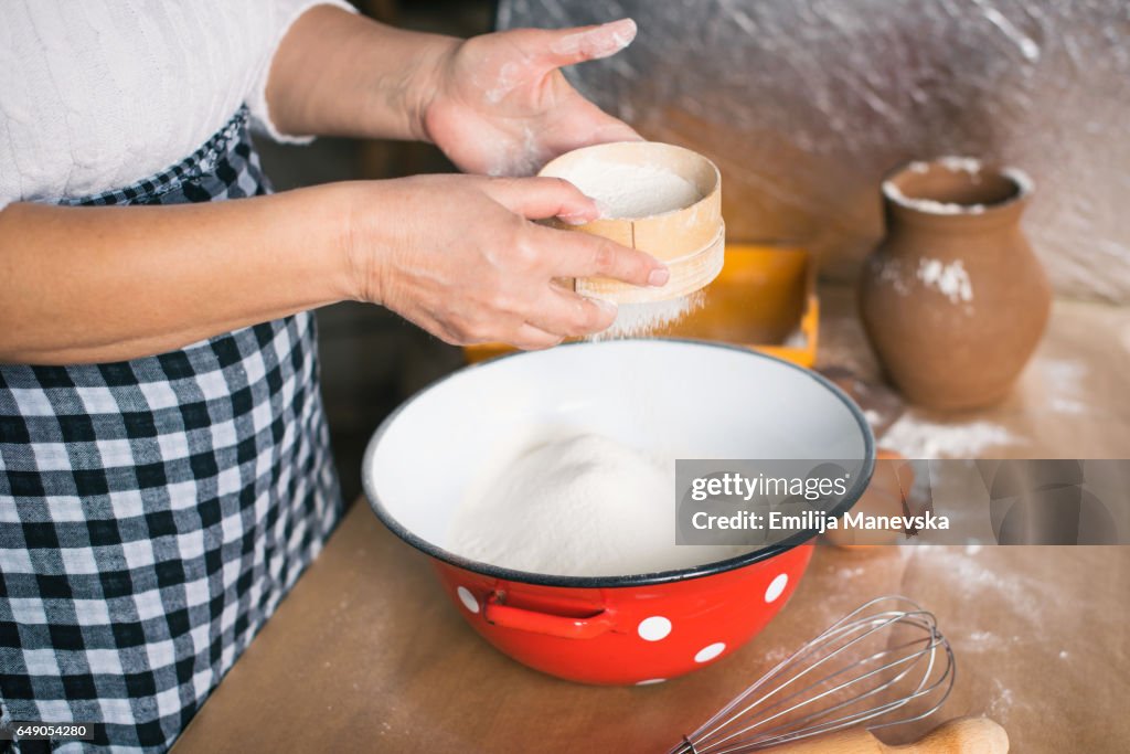 Woman sieving flour in domestic kitchen