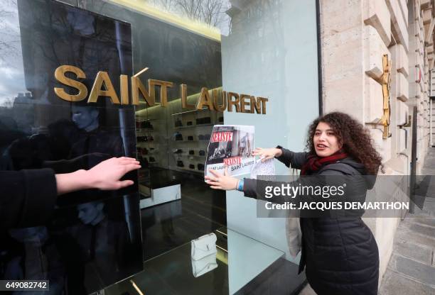 An activist of Effronte-e-s feminist movement puts a placard reading "sexist" on the window of a Yves Saint-Laurent shop in Paris on March 7, 2017...