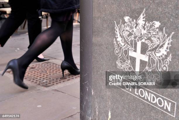 Businesswoman walks by a sign displaying the heraldic achievement of the City of London on March 7, 2017. - Britain's Finance minister Philip Hammond...