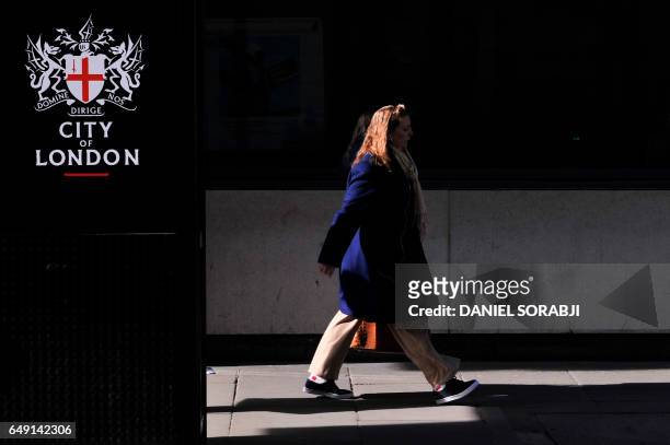 Businesswoman walks by a bus shelter with the heraldic achievement of the City of London printed on the side in the City of London on March 6, 2017....