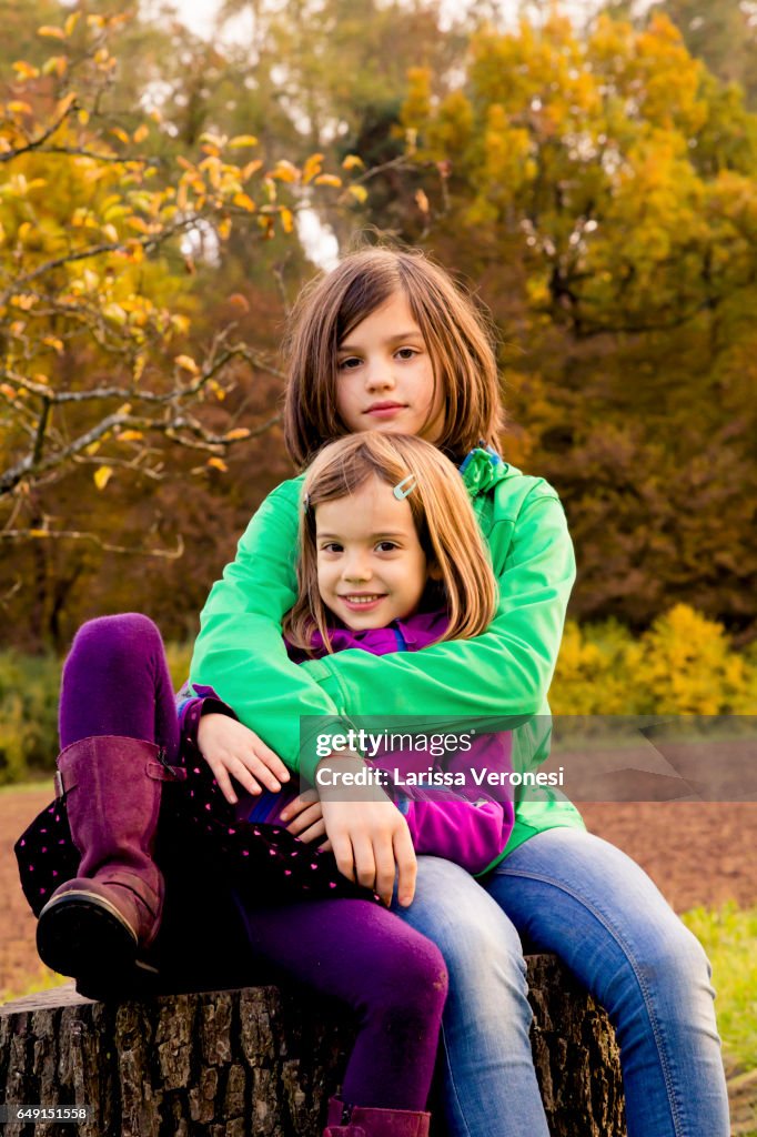 Two sisters sitting on a tree trunk