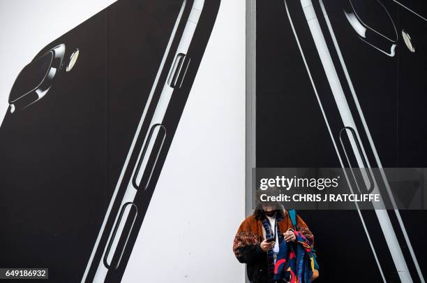 Man checks his phone next to billboards advertising the an Apple iPhone 7 smartphone as he stands on Oxford Street in London on March 7, 2017. -...