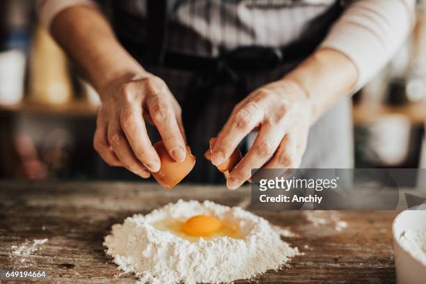 mujer añade un huevo a la harina - montar fotografías e imágenes de stock