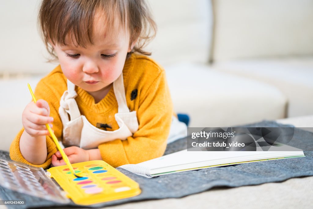 Three year old toddler painting a picture at home