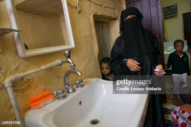 Matara stands with her children, in their run-down home, next to a sink that is not connected to running water, in a neighborhood in south Riyadh,...