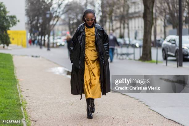 Michelle Elie wearing a mustard dress, vinyl coat outside Moncler on March 7, 2017 in Paris, France.
