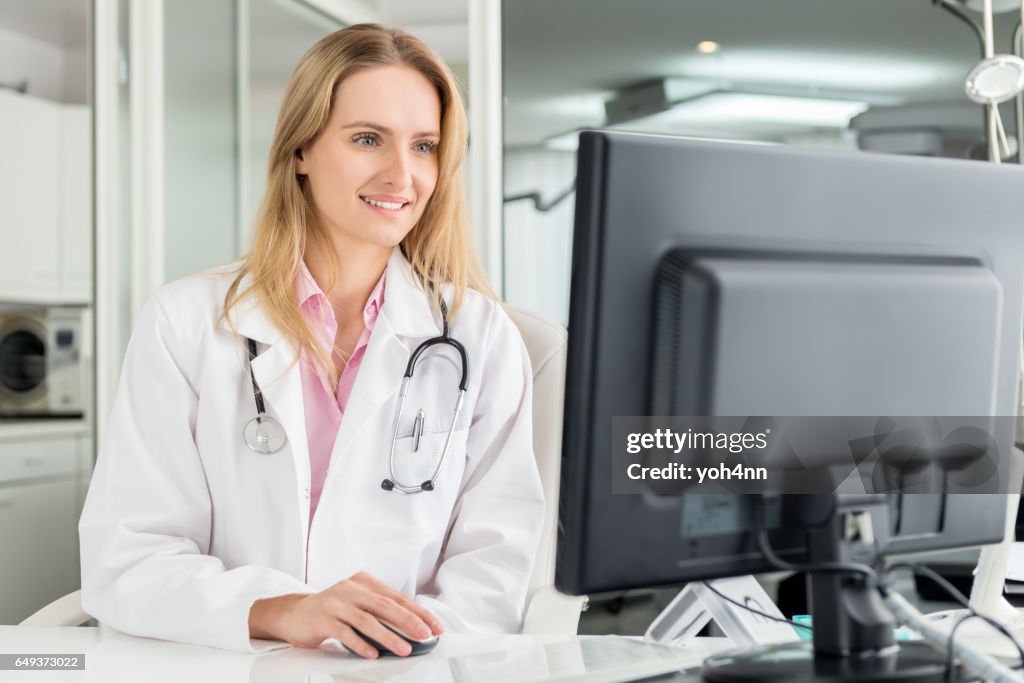 Médecin, assis au bureau & aide ordinateur