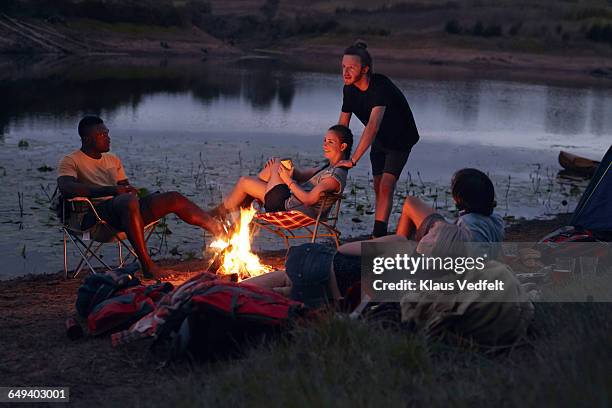 friends hanging out by bonfire on campsite - bon fire foto e immagini stock