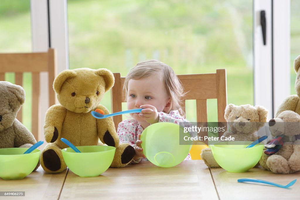 Toddler feeding teddy bears at table