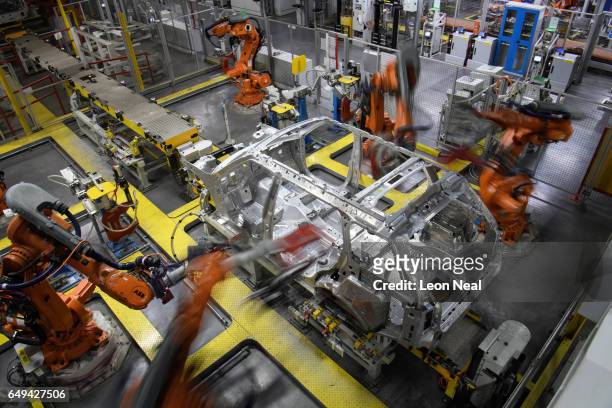 Robotic systems work on the chassis of a car during an automated stage of production at the Jaguar Land Rover factory on March 1, 2017 in Solihull,...