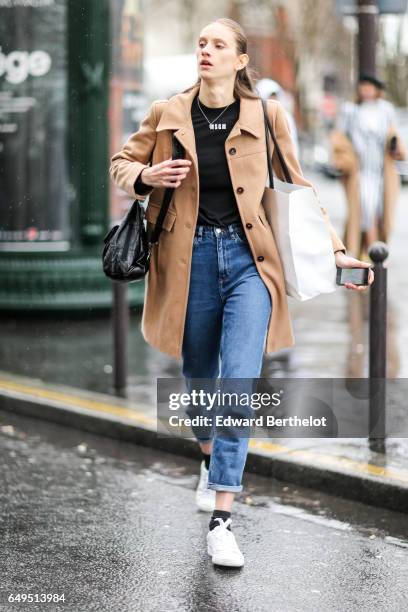 Model wears a brown coat, a black top, and blue jeans, outside the Celine show, during Paris Fashion Week Womenswear Fall/Winter 2017/2018, on March...