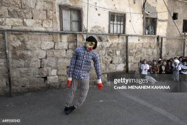 Ultra-Orthodox Jewish children wearing costumes look at a hanged figure doll symbolising the Evil Haman from the ancient Book of Ester, during their...