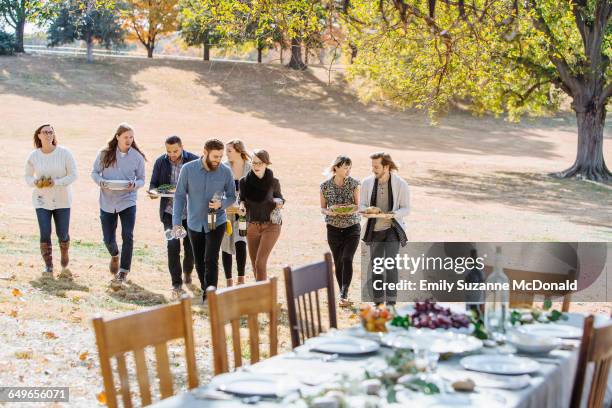 friends carrying food to outdoor table in rural field - röra mot bildbanksfoton och bilder