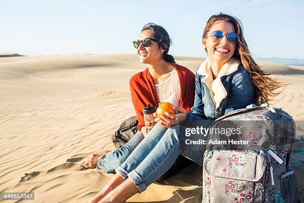 mixed race women sitting on sand dunes - sable ondulé photos et images de collection