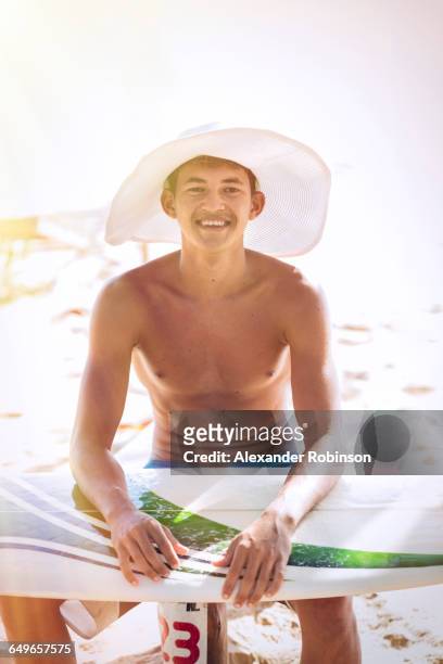mixed race teenage boy waxing surfboard on beach - brazilian waxing stockfoto's en -beelden