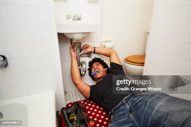 mixed race man fixing sink plumbing - schroevendraaier stockfoto's en -beelden