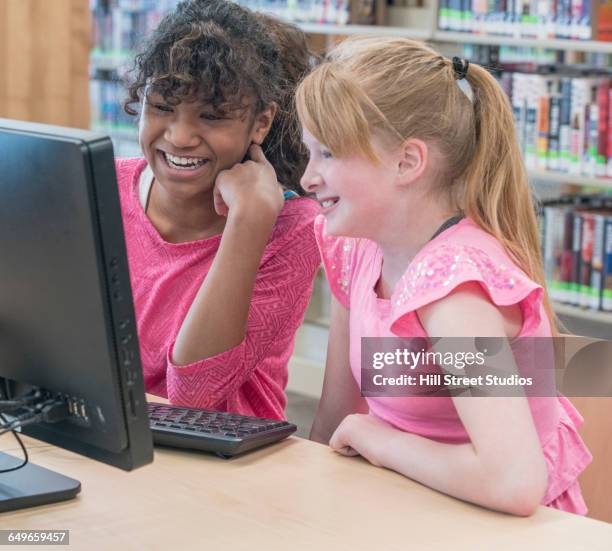 students using computer in library - girl 11 12 laughing close up foto e immagini stock