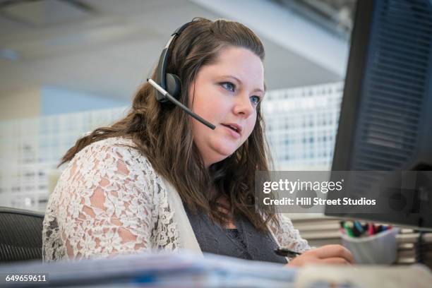 caucasian businesswoman talking on headset at office desk - headset imagens e fotografias de stock