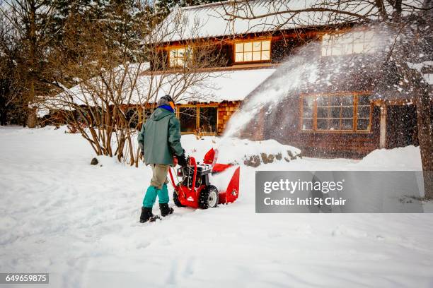caucasian man using snow blower in snowy driveway - quitanieves fotografías e imágenes de stock