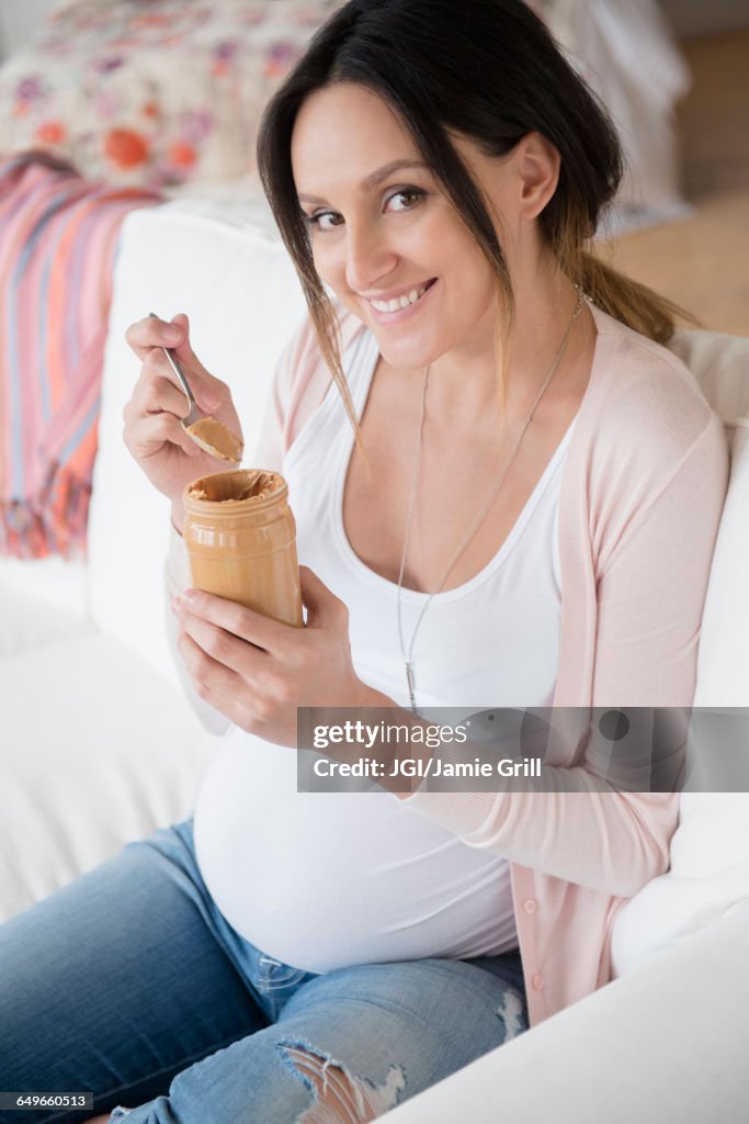 Pregnant Caucasian woman eating peanut butter from jar