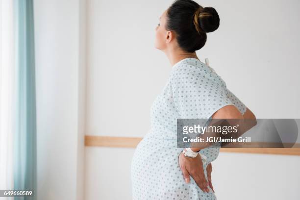 pregnant caucasian with back pain in hospital gown - giving birth stockfoto's en -beelden