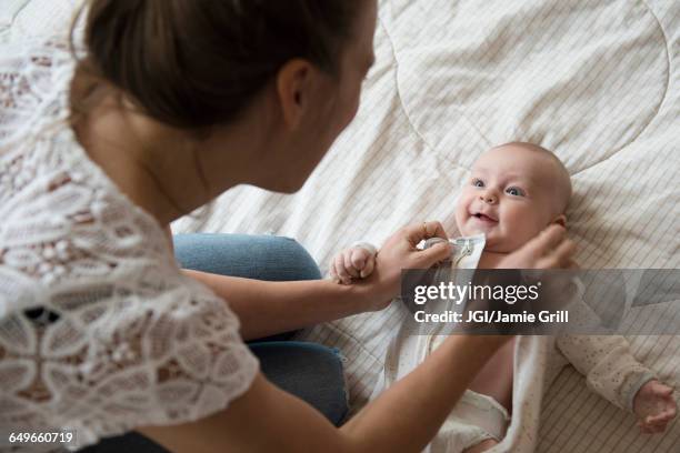caucasian mother dressing baby on bed - anziehen stock-fotos und bilder
