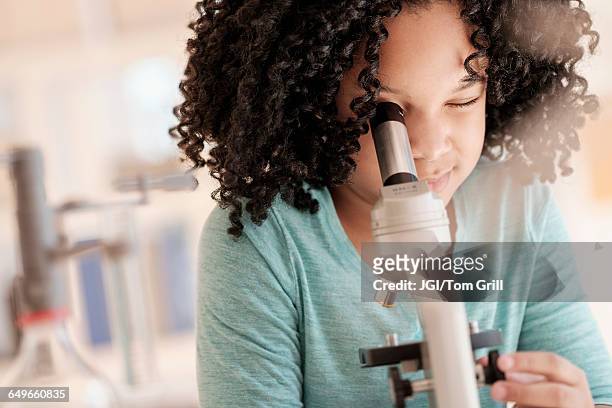 african american girl using microscope in science classroom - cientifico con microscopio fotografías e imágenes de stock