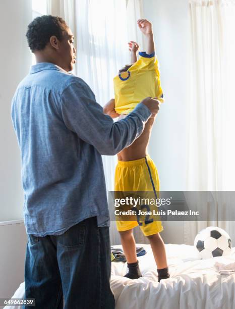 father dressing son in soccer uniform - fußballtrikot stock-fotos und bilder