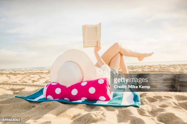 caucasian woman reading book on beach - woman towel beach stockfoto's en -beelden