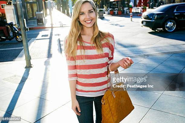 caucasian woman smiling on city sidewalk - sac à main blanc photos et images de collection
