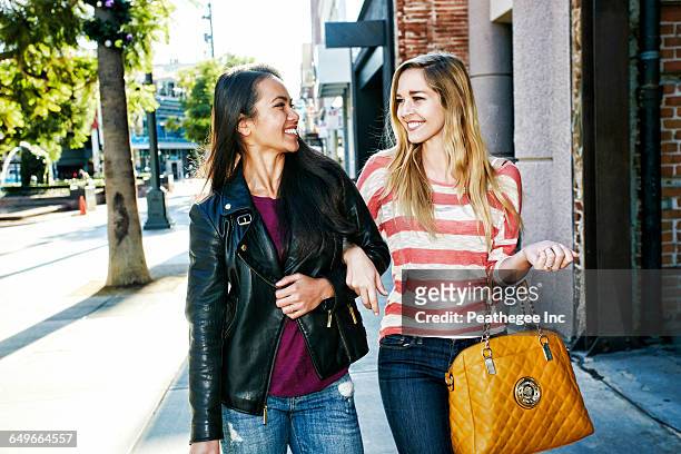 women walking arm-in-arm on sidewalk - sac à main blanc photos et images de collection
