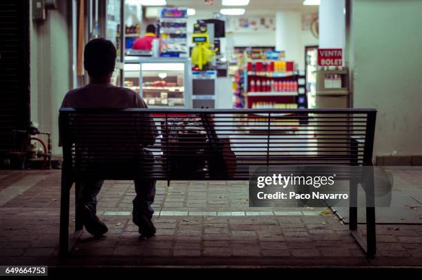 man sitting on city bench at night - gemakswinkel stockfoto's en -beelden