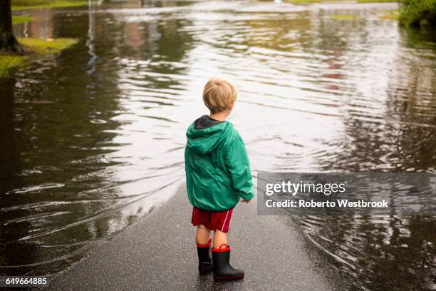 caucasian boy wearing puddles near flood - naturkatastrophe stock-fotos und bilder