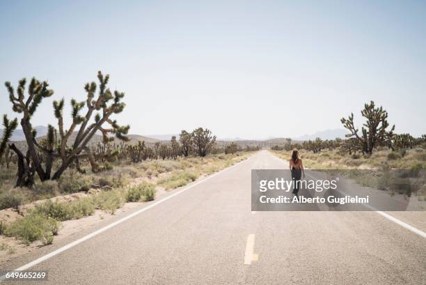 caucasian woman walking on remote desert road - nevada stock-fotos und bilder