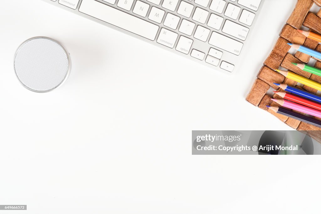 Bluetooth portable speaker with computer keyboard, colour pencils on white office desk